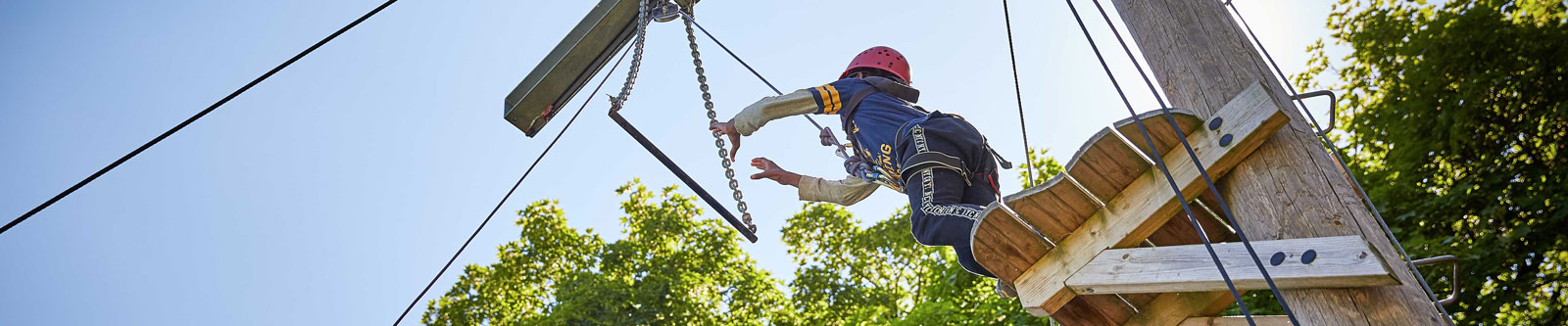 A young boy jumping off a high wooden platform to reach a trapeze bar